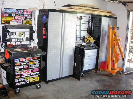 Garage interior with tool chest, storage cabinets, chop saw, and engine hoist