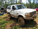 1996 Ford Bronco - A heavily modified 1996 Ford Bronco sits in a muddy, wooded setting, with another red vehicle visible in the background.