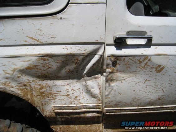 White 1996 Ford Bronco side door and fender heavily dented and covered in mud