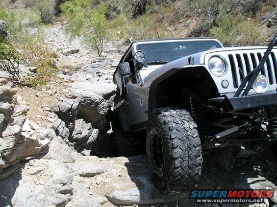 Silver Jeep Wrangler on rocky terrain, front 3/4 view, off-road tires