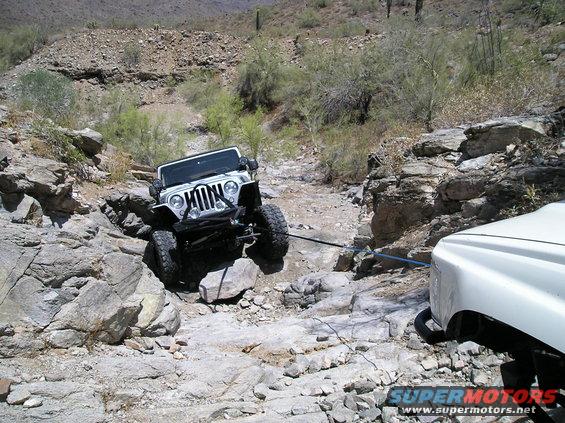 White Jeep Wrangler on a rocky trail, being pulled by another vehicle. Desert landscape