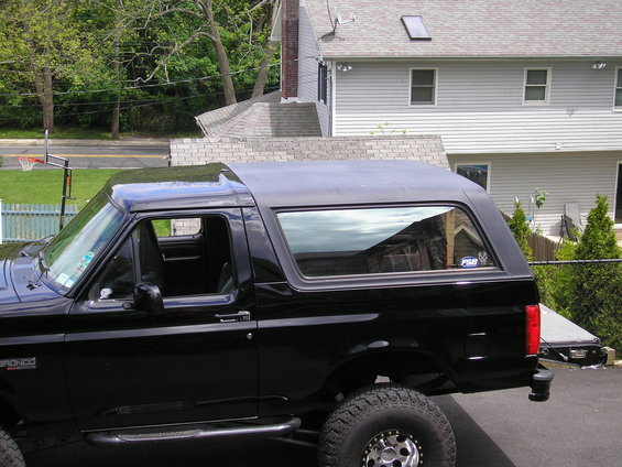 Black Ford Bronco parked in a driveway, side view. Has a removable top