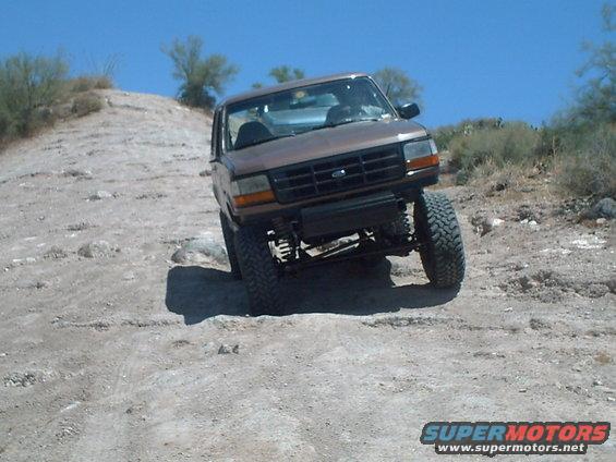 Brown Ford Bronco with lifted suspension driving on a dirt hill