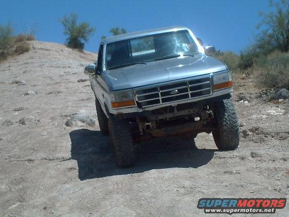 Silver pickup truck with lifted suspension driving on a dirt hill