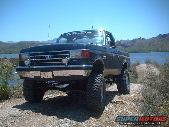 1991 Ford Bronco lifted with off-road tires parked by a lake