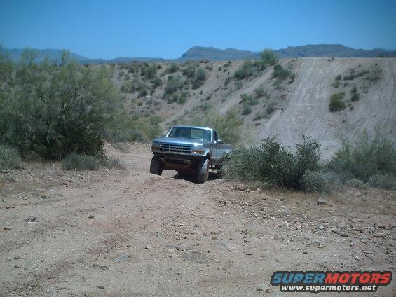 Silver pickup truck with lifted suspension driving on a dirt road in a desert landscape