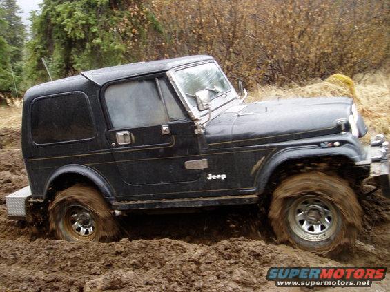 Black Jeep stuck in thick mud, tires spinning