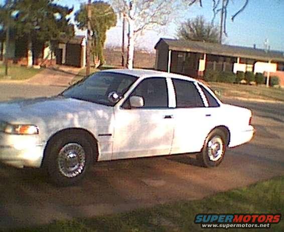 White sedan parked on a dirt road in front of some buildings