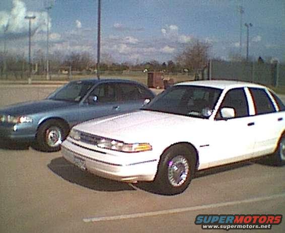 White 1995 Ford Crown Victoria parked next to a blue sedan, front 3/4 view, showing grille and headlights