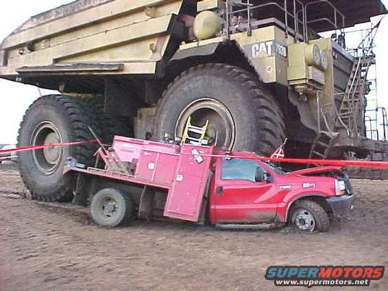 Red pickup truck dwarfed by a massive yellow CAT mining truck