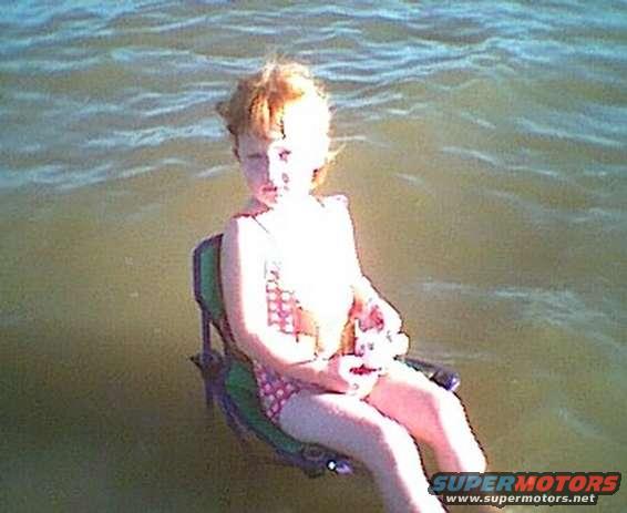 Child in a chair in water, holding a toy