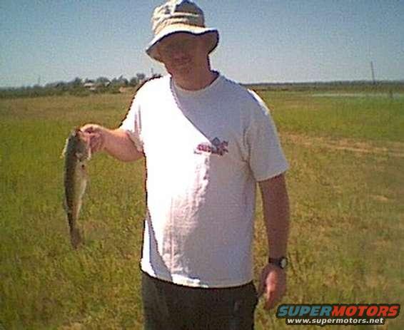 Man in a hat and t-shirt holding a fish in a grassy field