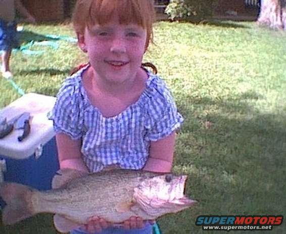 Girl in blue checkered shirt holds a large fish in front of a cooler