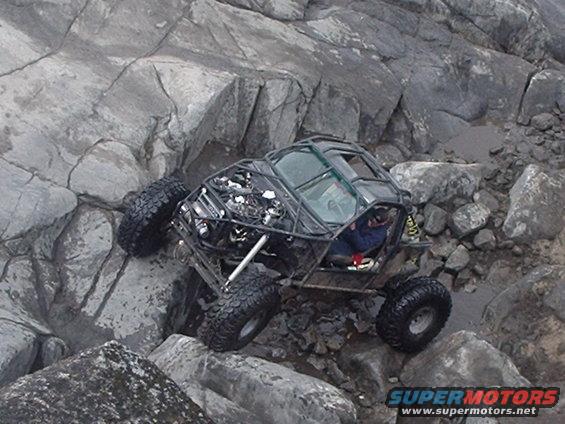 Off-road buggy with large tires driving over rocks.