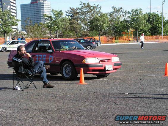 Red 1990 Ford Mustang coupe with blue racing numbers '338-D' and '5.0' badge, parked on asphalt with orange cones