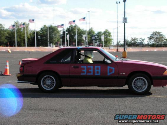 Red 1990 Ford Mustang coupe with blue racing numbers 338 D on the door, driver wearing a helmet