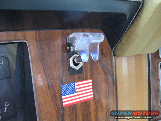 Dashboard interior with wood grain paneling, a toggle switch, and an American flag sticker. Supermotors.net logo visible