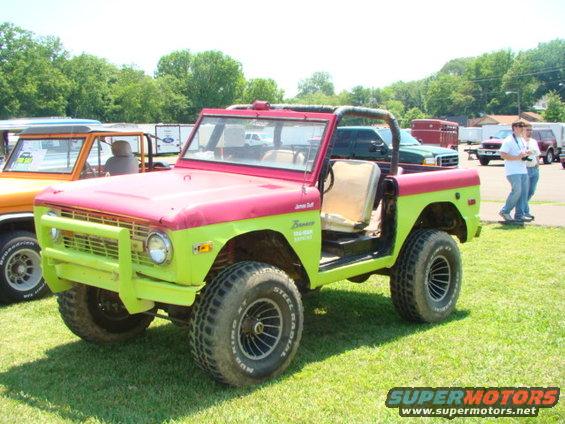 Two-tone red and lime green Ford Bronco with aftermarket bumper and roll cage. Another Bronco is parked to its left