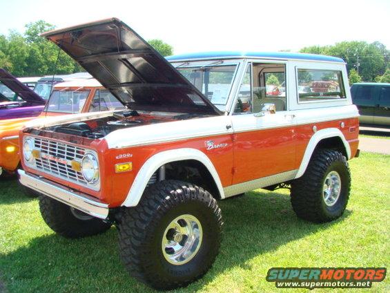 Orange and white Ford Bronco with hood open, lifted suspension, and large tires