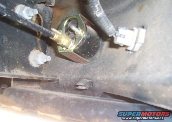 Close-up of a metal bracket with a cable and electrical connector attached to a vehicle's frame