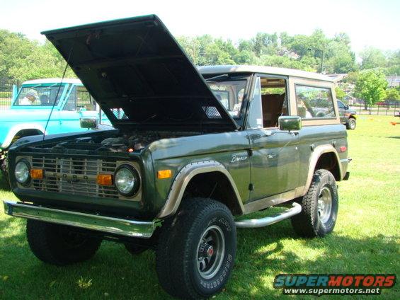 Green 1978 Ford Bronco with hood open, parked on grass next to a blue vehicle