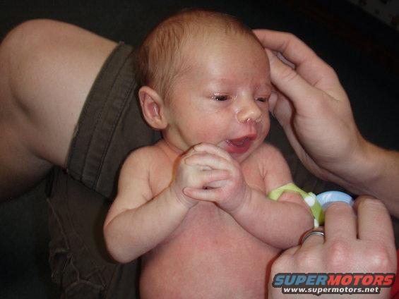 Newborn baby held by adults, wearing a yellow band on its arm