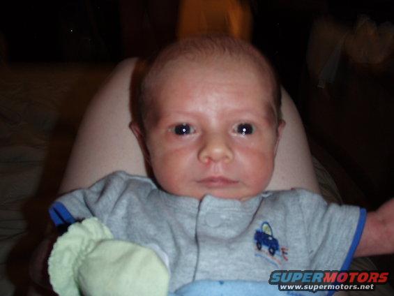 Baby wearing a gray onesie with a blue car graphic, held by an adult