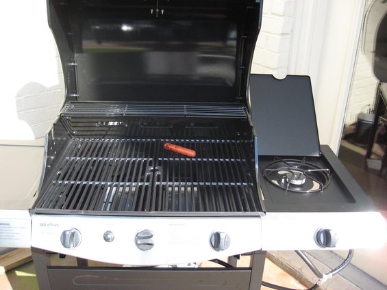 Gas grill with one hot dog on the grates and a side burner