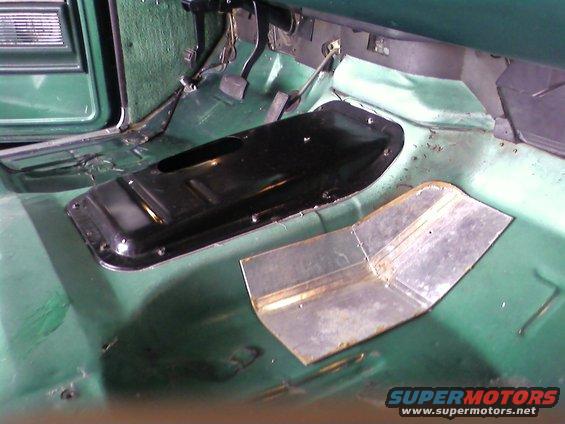 Green vehicle interior floor with black transmission tunnel cover and metal patch