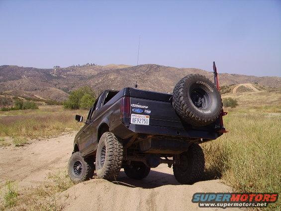 Black Ford Bronco II with spare tire on back, driving on dirt road in hills
