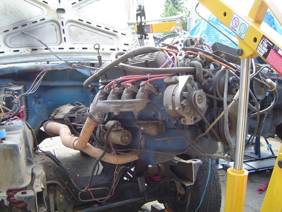engine hoist lifting out a blue engine from a vehicle, wires and hoses disconnected