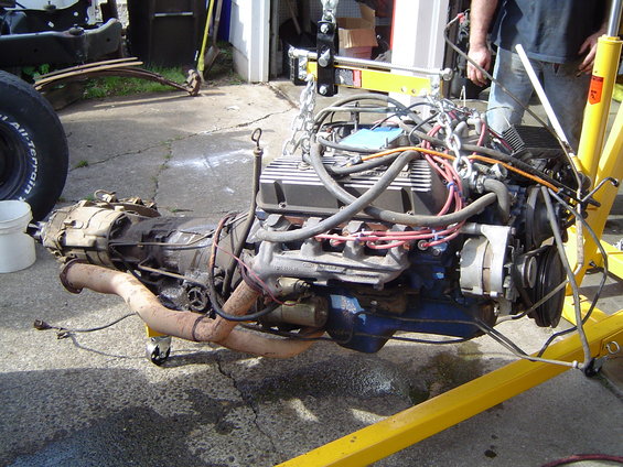 Engine and transmission assembly on an engine stand, with exhaust manifolds and alternator visible