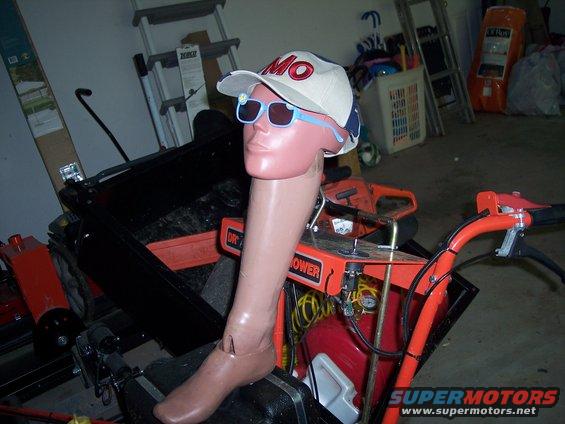 Mannequin leg and torso wearing a hat and sunglasses, seated on equipment