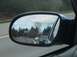 1996 Chevrolet Impala - View of highway traffic reflected in a side mirror, with trees and clouds visible in the background.