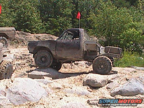 Mud-covered pickup truck with a red flag on its roof, navigating rocky terrain