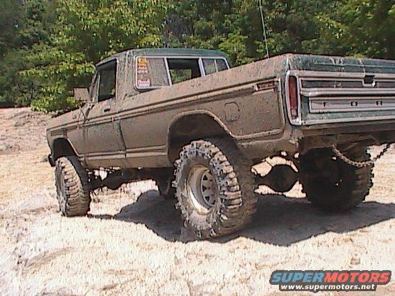 Mud-covered pickup truck with large off-road tires, seen from the rear three-quarter view. The truck appears to be from the 1970s