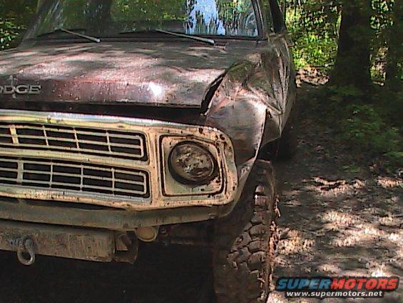 Front view of a damaged Dodge pickup truck with a dented fender and grille. Off-road tires are visible