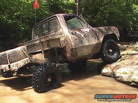 Mud-covered pickup truck with camouflage paint, off-roading through water and rocks
