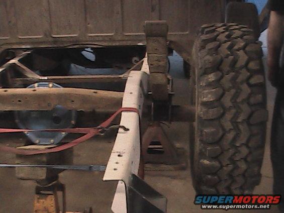 Truck chassis on jack stands with a large off-road tire visible on the right