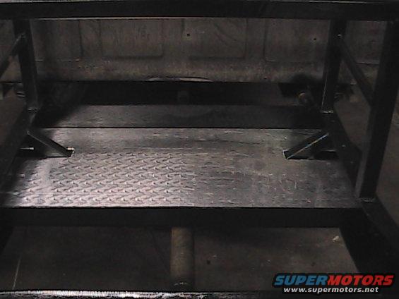 Truck bed interior with diamond plate flooring and black metal frame structure. Supermotors.net logo visible
