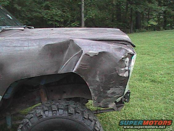 Damaged dark-colored truck fender and hood, off-road tire visible