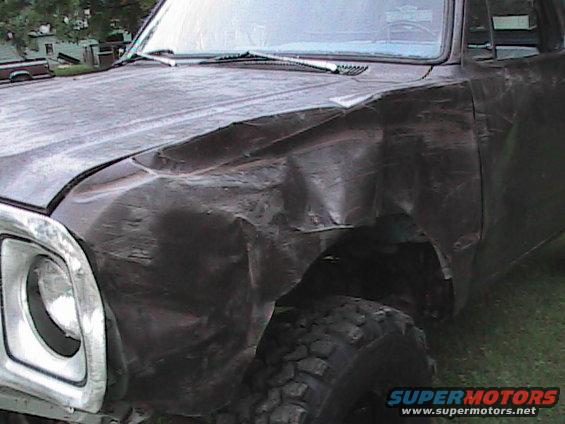 Damaged dark colored truck fender and hood with chrome headlight bezel. Off-road tire visible