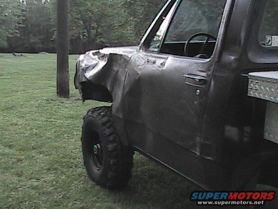 Pickup truck with heavily damaged front fender and door. It has large off-road tires