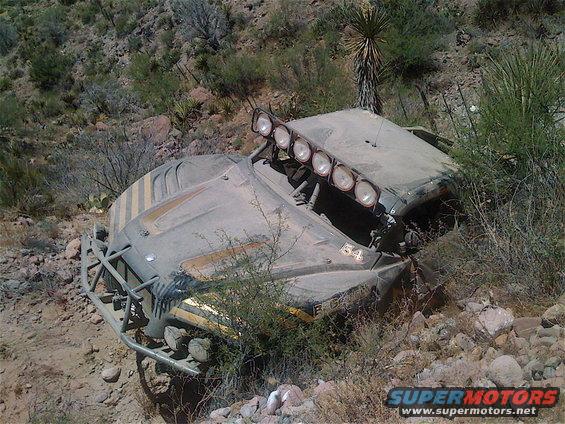 Off-road buggy with six lights on roof, crashed on rocky hillside. Number 54 visible on hood