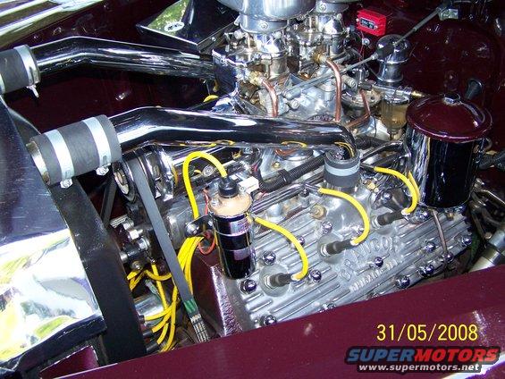 Close-up of a V8 engine with chrome intake pipes, dual carburetors, and yellow spark plug wires