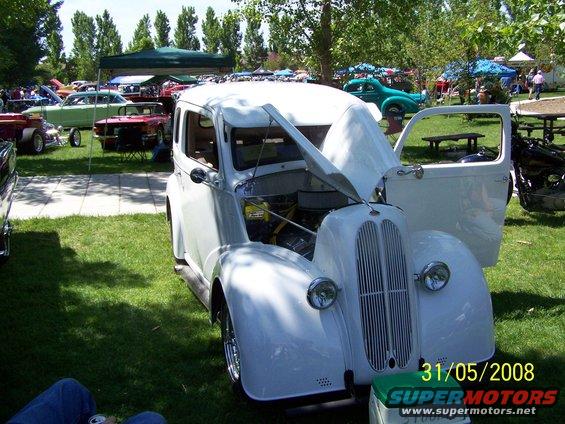 White sedan with hood and door open at a car show, showing engine details