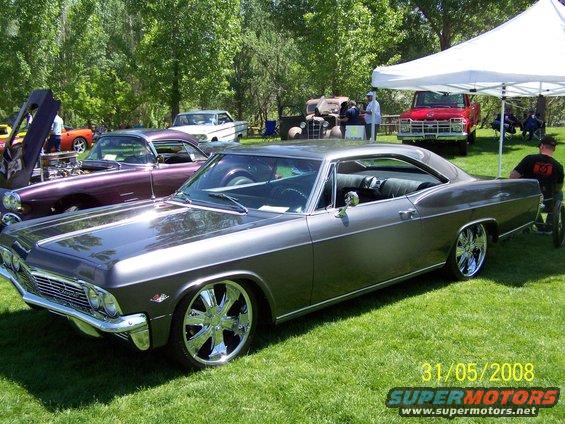 1965 Chevrolet Impala with custom wheels parked on grass, other cars and tents in background