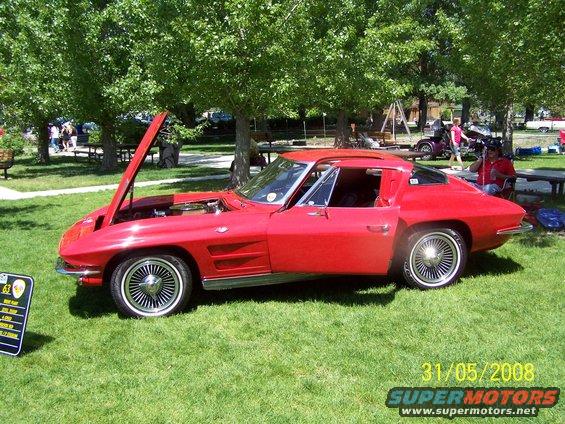 red 1963 Corvette Sting Ray coupe, hood open, parked on grass at an outdoor event