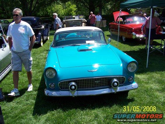 Blue convertible car, front view, with a man standing to the left