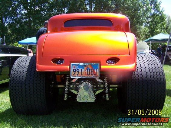 Rear view of an orange hot rod coupe with large rear tires and a license plate